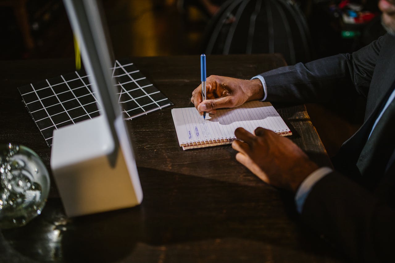 about-us A businessman in a suit writing notes on a notebook at a desk, suggesting a professional office environment.