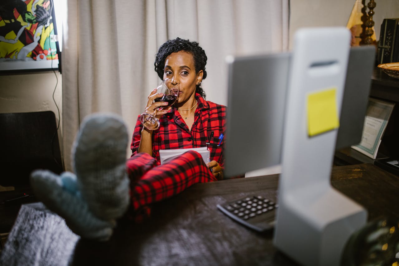services-04 Woman in red pajamas relaxing with wine at a home office desk with feet up.